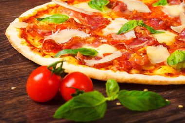 Erimiş mozzarella, parmezan peyniri, salam, kırmızı kiraz domates ve taze yeşil fesleğen ile pizza Italyan mozzarella, kırmızı tatlı biber, kiraz ve haddeleme pin ile dekore kahverengi bir masada yaprakları