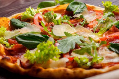 Mozzarella, parmezan peyniri, kırmızı domates ve taze yeşil fesleğen, roka ve lahana yaprakları mozzarella, kırmızı biber, kiraz ve haddeleme pin tarafından dekore edilmiş kahverengi bir masada yakın yukarı Pizza İtalyan