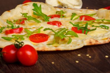 Erimiş mozzarella, parmezan peyniri, kırmızı domates ve taze yeşil roka yaprakları ile Vejetaryen İtalyan Pizza mozzarella, kırmızı tatlı biber, kiraz domates ile süslenmiş kahverengi bir masa üzerinde