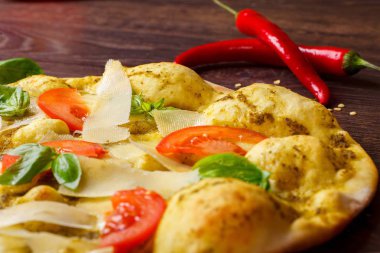 Erimiş mozzarella, parmezan peyniri, kırmızı domates ve taze yeşil fesleğen ile vejetaryen Italyan pizzası, mozzarella, kırmızı tatlı biber, kiraz domates ile süslenmiş kahverengi bir masada yaprakları. Yakın çekim