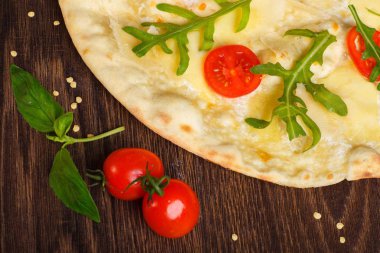 Erimiş mozzarella, parmezan peyniri, kırmızı domates ve taze yeşil roka yaprakları ile Vejetaryen İtalyan Pizza mozzarella, kırmızı tatlı biber, kiraz domates ile süslenmiş kahverengi bir masa üzerinde