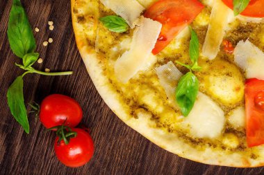 Erimiş mozzarella, parmezan peyniri, kırmızı domates ve taze yeşil fesleğen ile vejetaryen Italyan pizzası, mozzarella, kırmızı tatlı biber, kiraz domates ile süslenmiş kahverengi bir masada yaprakları. Yakın çekim