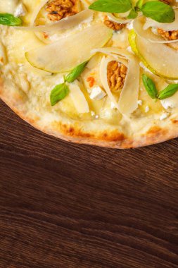 Fındık, sarı armut, parmesan peyniri ve taze yeşil fesleğen ile vejetaryen Italyan pizza mozzarella, kırmızı sıcak biber, kiraz domates ile süslenmiş kahverengi bir masada yaprakları. Üst görünüm. Yakın çekim
