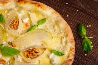 Fındık, sarı armut, parmesan peyniri ve taze yeşil fesleğen ile vejetaryen Italyan pizza mozzarella, kırmızı sıcak biber, kiraz domates ile süslenmiş kahverengi bir masada yaprakları. Üst görünüm. Yakın çekim