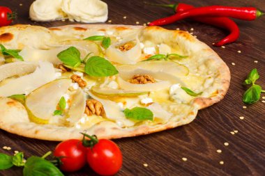 Fındık, sarı armut, parmesan peyniri ve taze yeşil fesleğen ile vejetaryen Italyan pizza mozzarella, kırmızı sıcak biber, kiraz domates ve haddeleme pin tarafından dekore kahverengi bir masada yaprakları