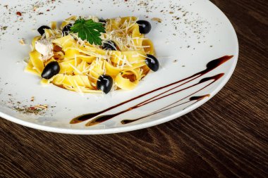 Parmesan tarafından dekore edilmiş kahverengi ahşap bir masada sos ile süslenmiş büyük beyaz bir çanak siyah zeytin, peynir ve yeşil yaprak ile taze Italyan makarna