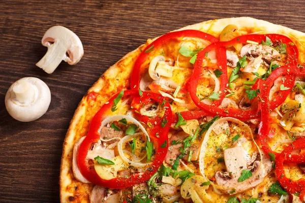 Cerrar pizza italiana con queso derretido, tomates rojos, pimienta, champiñones, cebolla y hierbas en una mesa marrón decorada con champiñones, pimiento dulce rojo y tomates cherry — Foto de Stock