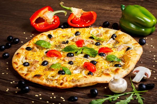 Primer plano de atún vegetariano Pizza italiana queso derretido, aceitunas negras, tomates cherry rojos y hojas de albahaca verde fresca en una mesa marrón decorada con setas, aceitunas negras, pimiento rojo y rúcula fresca — Foto de Stock