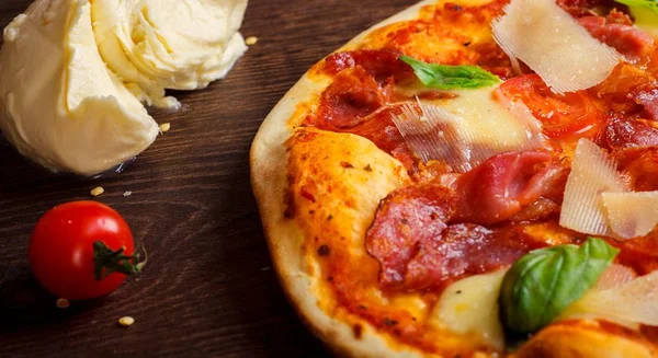 Pizza italiana con mozzarella fusa, parmezan, salame, pomodorini rossi e foglie di basilico verde fresco su un tavolo marrone decorato con mozzarella, peperone rosso dolce, ciliegia e mattarello — Foto Stock