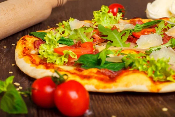 Närbild pizza italienska med mozzarella, och parmesanost ost, röda tomater och färsk grön basilika, ruccola och kål blad på ett brunt bord dekorerad med mozzarella, röd paprika, körsbär och brödkavel — Stockfoto