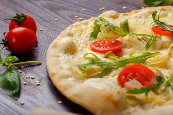 Vegetarisk italiensk pizza med smält mozzarella, och parmesanost ost, röda tomater och färska gröna ruccola blad på ett brunt bord dekorerad med mozzarella, röd paprika, körsbärstomater — Stockfoto