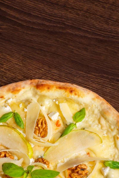 Fındık, sarı armut, parmesan peyniri ve taze yeşil fesleğen ile vejetaryen Italyan pizza mozzarella, kırmızı sıcak biber, kiraz domates ile süslenmiş kahverengi bir masada yaprakları. Üst görünüm. Yakın çekim