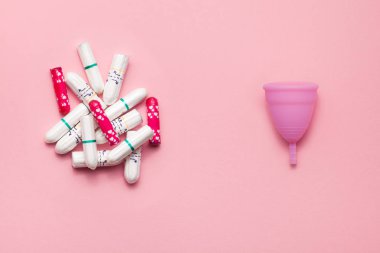 Yumuşak pembe arka planda yeniden kullanılabilir silikon menstrüel fincan ve tamponlar karşılaştırma yığını. Modern kadın samimi alternatif jinekolojik hijyen. Eko sıfır atık kavramı