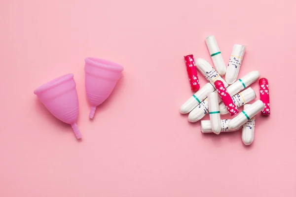 Två återanvändbara silikon menstruations koppar och hög med tamponger jämförelse på en mjuk rosa bakgrund. Modern kvinnlig intim alternativ gynekologisk hygien. Eco Zero avfall koncept Stockbild