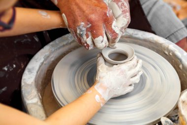 Çömlekçiliği kapatın. Yetişkin çömlekçi çamurlu elleri bir tekerlek üzerinde kil ile yardımcı olmak için çocuk elleri rehberlik