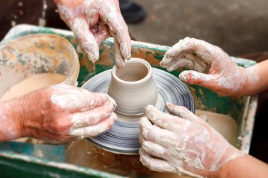 Çömlekçiliği kapatın. Yetişkin çömlekçi çamurlu elleri bir tekerlek üzerinde kil ile yardımcı olmak için çocuk elleri rehberlik