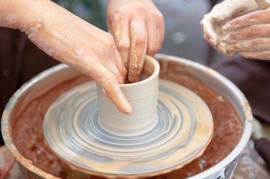 Çömlekçiliği kapatın. Yetişkin çömlekçi çamurlu elleri bir tekerlek üzerinde kil ile yardımcı olmak için çocuk elleri rehberlik