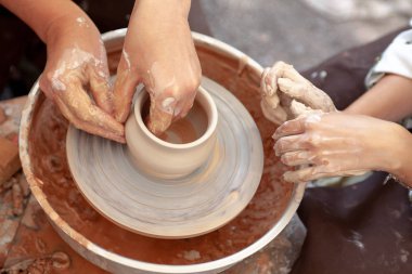 Çömlekçiliği kapatın. Yetişkin çömlekçi çamurlu elleri bir tekerlek üzerinde kil ile yardımcı olmak için çocuk elleri rehberlik