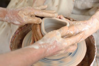 Çömlekçiliği kapatın. Yetişkin çömlekçi çamurlu eller bir tekerlek üzerinde kil ile yardımcı olmak için öğrencilere elleri rehberlik