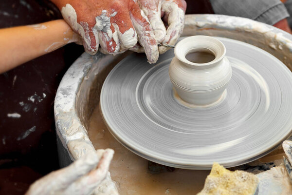 Close up pottery. Adult potter muddy hands guiding child hands to help with clay on a wheel
