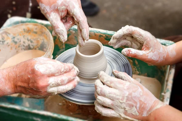 Çömlekçiliği kapatın. Yetişkin çömlekçi çamurlu elleri bir tekerlek üzerinde kil ile yardımcı olmak için çocuk elleri rehberlik