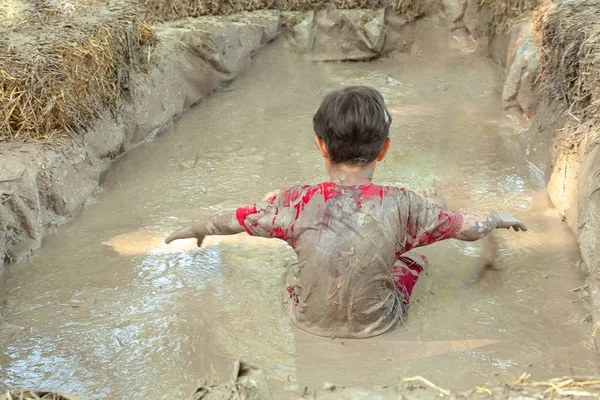 Heureux garçon totalement sale est assis et jouer dans un bassin de boue improvisé boueux liquide potier argile. Amusez-vous bien dehors. Concept d'enfance heureuse Image En Vente