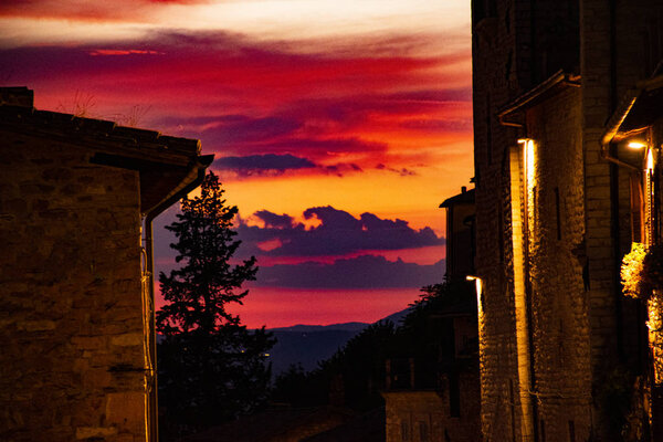 Exciting sunset full of colors in the town of Assisi among old stone houses and trees in the beautiful Umbria in central Italy