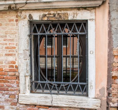 Venedik, İtalya 'da parmaklıkları olan oval bir pencerenin camlarında şehrin yansımaları.