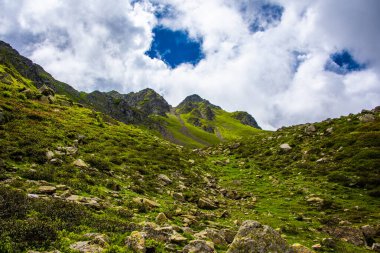 Beyaz bulutlar, mavi gökyüzü, yeşil çayırlar ve bir yaz günü Levico Gölü yakınlarındaki Trentino Alpleri 'ndeki Lagorai' de granit kayalar.