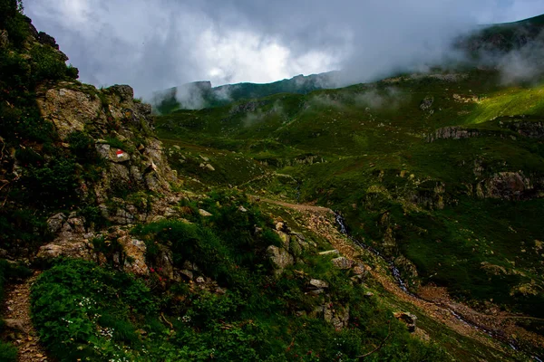 path climbs between the alpine and granite rocks of Lagorai with cloudy skies near Lake Levico in Trento, Italy