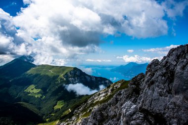 İtalya 'nın Trento kentindeki Monte Altissimo di Nago' da kayalar, bulutlar ve mavi gökyüzü arasındaki Garda Gölü manzarası