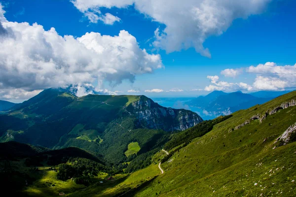 İtalya, Trento 'daki Monte Altissimo di Nago' dan mavi gökyüzünde yeşil çayırları ve bulutları olan Monte Baldo 'nun güzel manzarası.