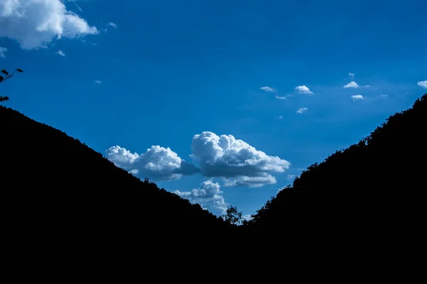 蓝天上美丽的云彩似乎被描绘在两座山的轮廓之间 — 图库照片