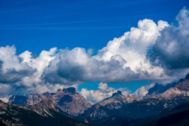Cortina D 'Ampezzo' nun etrafındaki Dolomitler beyaz bulutlarla çevrili mavi gökyüzüne karşı dururlar. Cortina D 'Ampezzo, Belluno, İtalya' daki Sorapis Gölü etrafındaki orman.