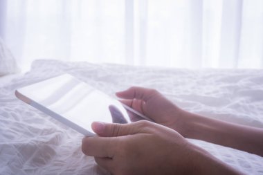 Kadın el tablet tutmak, gölge yansıtır ekranda beyaz yorgan ile yatak, sabah doğal ışık penceresinden uzanarak ederken. Kavramları iletişim ağı, dijital teknoloji, online eğitim.