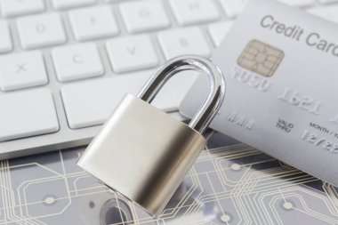 Gri kredi kartı, beyaz klavye ve arka plan üzerinde elektronik devreler ile Metal asma kilit. Online alışveriş, veri şifreleme, siber güvenlik ve finansal işlem kavramları.