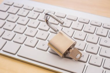 Beyaz klavyeden, ahşap masa arka plan üzerine açık metal asma kilit. Çatlama şifre, şifreleme, internet erişimi, siber ağ, iş çözümü, blockchain hareket kavramları.