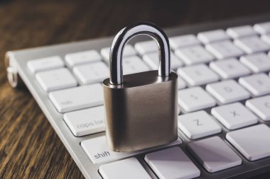 Modern beyaz klavye asma kilit anahtar arka plan üzerinde ahşap masa ile yakın, hafif koyu tonu dim. Dijital veri koruması, internet erişimi, siber ağ, şifre güvenliği, online iş kavramları.