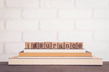 INSURANCE kelimesi, kitapların üstündeki blok küplere yazılmış harfler ve tuğla kaplamalı ahşap masa, boş fotokopi alanı, klasik asgari tarz. İş ve hayat kaybından korunma kavramları.