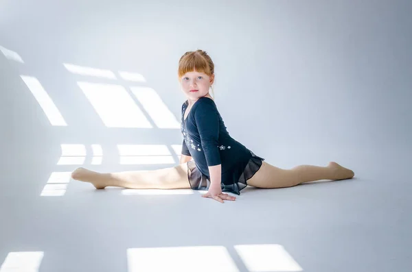 La bambina esegue uno spago da ginnastica in studio su uno sfondo bianco. Il concetto di fitness e sport e uno stile di vita sano — Foto Stock