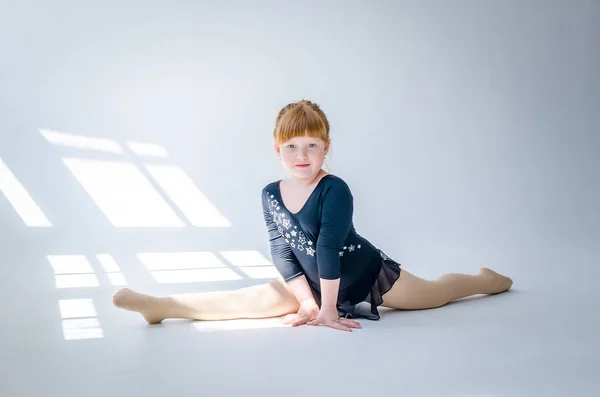 La bambina esegue uno spago da ginnastica in studio su uno sfondo bianco. Il concetto di fitness e sport e uno stile di vita sano — Foto Stock