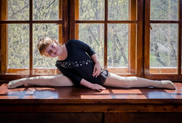 Uma garotinha faz um cordel de ginástica sentado no peitoril da janela. O conceito de fitness e desporto e um estilo de vida saudável — Fotografia de Stock
