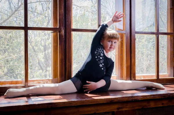 Uma garotinha faz um cordel de ginástica sentado no peitoril da janela. O conceito de fitness e desporto e um estilo de vida saudável — Fotografia de Stock