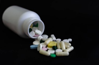 Kavanozdan siyah bir arka plan üzerine dökülen tıbbi tabletler.