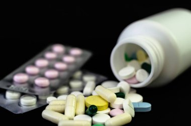 Kavanozdan siyah bir arka plan üzerine dökülen tıbbi tabletler.