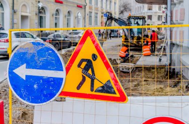 Yol tamiri. Yol işaretleri yol onarımları ve farklı bir rota seçimi hakkında uyarı. Arka planda onarım işlemi