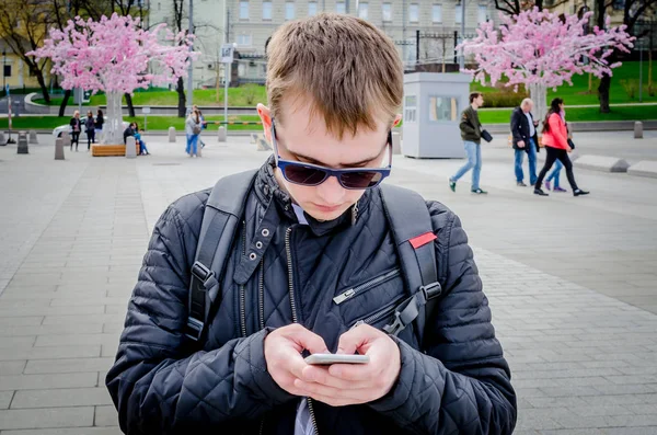 A young man looking at the city street with enthusiasm in the smartphone screen. A passion for technology and news. Lack of attention on the streets of the city because of the smartphone. — Stock Photo, Image