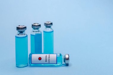 Mavi arka planda cam şişelerde Coronavirus aşısı
