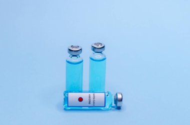 Mavi arka planda cam şişelerde Coronavirus aşısı