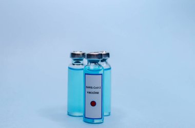 Mavi arka planda cam şişelerde Coronavirus aşısı